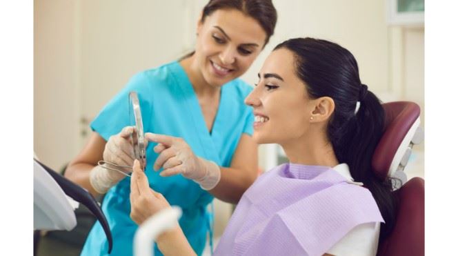 person looking at cleaned teeth in dental office with assistant